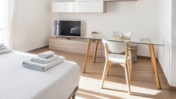 Una habitación de hotel moderna con una cama, un televisor, una mesita de vidrio y una silla.