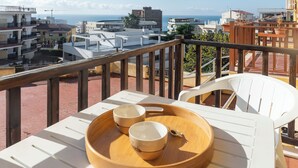Un balcón con una bandeja de madera que sostiene dos tazas, con vista a una ciudad costera con edificios y el mar.