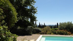 A swimming pool surrounded by gravel, with trees and shrubs in the background.