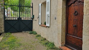 A stone building with a wooden door and shutters, a metal gate, and a small garden area.