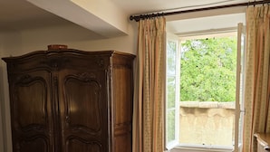 A room with a large wooden cabinet, a window with curtains, and a tiled floor.