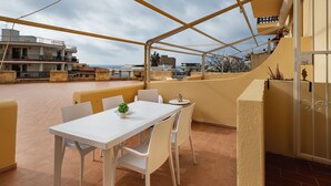 Une terrasse avec une table et des chaises blanches, un pot de fleurs et une vue sur le paysage urbain.