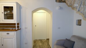 A hallway with a white door, a wooden cabinet with dishes, and a beige sofa.