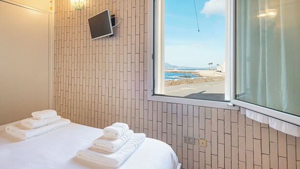 Ein Hotelzimmer mit Bett, einem an der Wand montierten Fernseher und einem Fenster mit Meerblick.