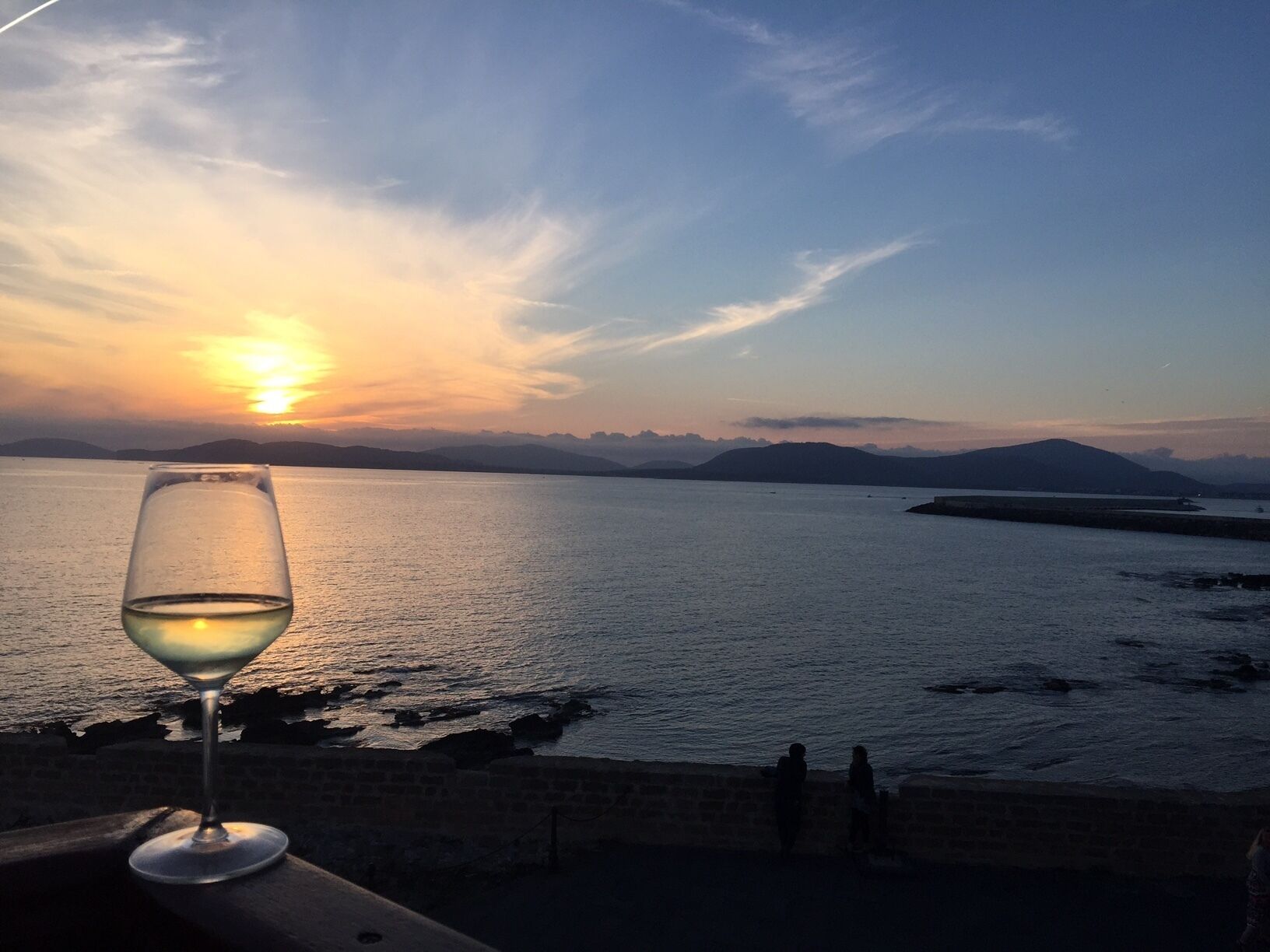 A sunset view over a body of water with a glass of white wine on a balcony.