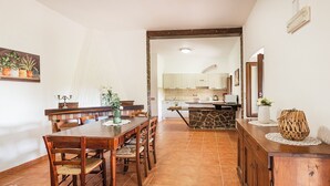 Un comedor con una mesa y sillas de madera, una cocina al fondo y una planta decorativa en la pared.