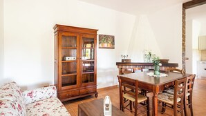 Un comedor con una mesa y sillas de madera, un sofá floral y un aparador de madera con puertas de cristal.