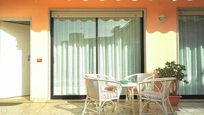 A room with two wicker chairs and a table, a potted plant, and a sliding glass door with a curtain.