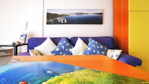 A room with a purple sofa, a wooden table, and a painting of a coastal landscape.