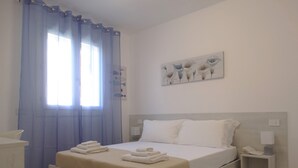 A neatly arranged bedroom with a bed, a bedside table, a nightstand, and a window with curtains. - Prestigiosa - Two Bedroom Apartment, Sleeps 5 (Alghero)