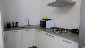 A modern kitchen with white cabinets, a stainless steel sink, a kettle, a microwave, and a gas stove. - Prestigiosa - Two Bedroom Apartment, Sleeps 5 (Alghero)