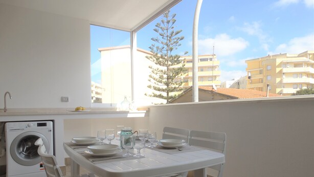A balcony with a table set for dining, a washing machine, and a view of buildings. - Prestigiosa - Two Bedroom Apartment, Sleeps 5 (Alghero)
