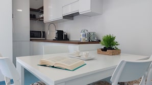 A modern kitchen with white cabinetry, a microwave, a coffee maker, and a potted plant on the counter.