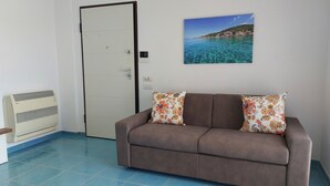 A room with a brown sofa, two floral cushions, a door, and a wall-mounted picture of a coastal landscape.