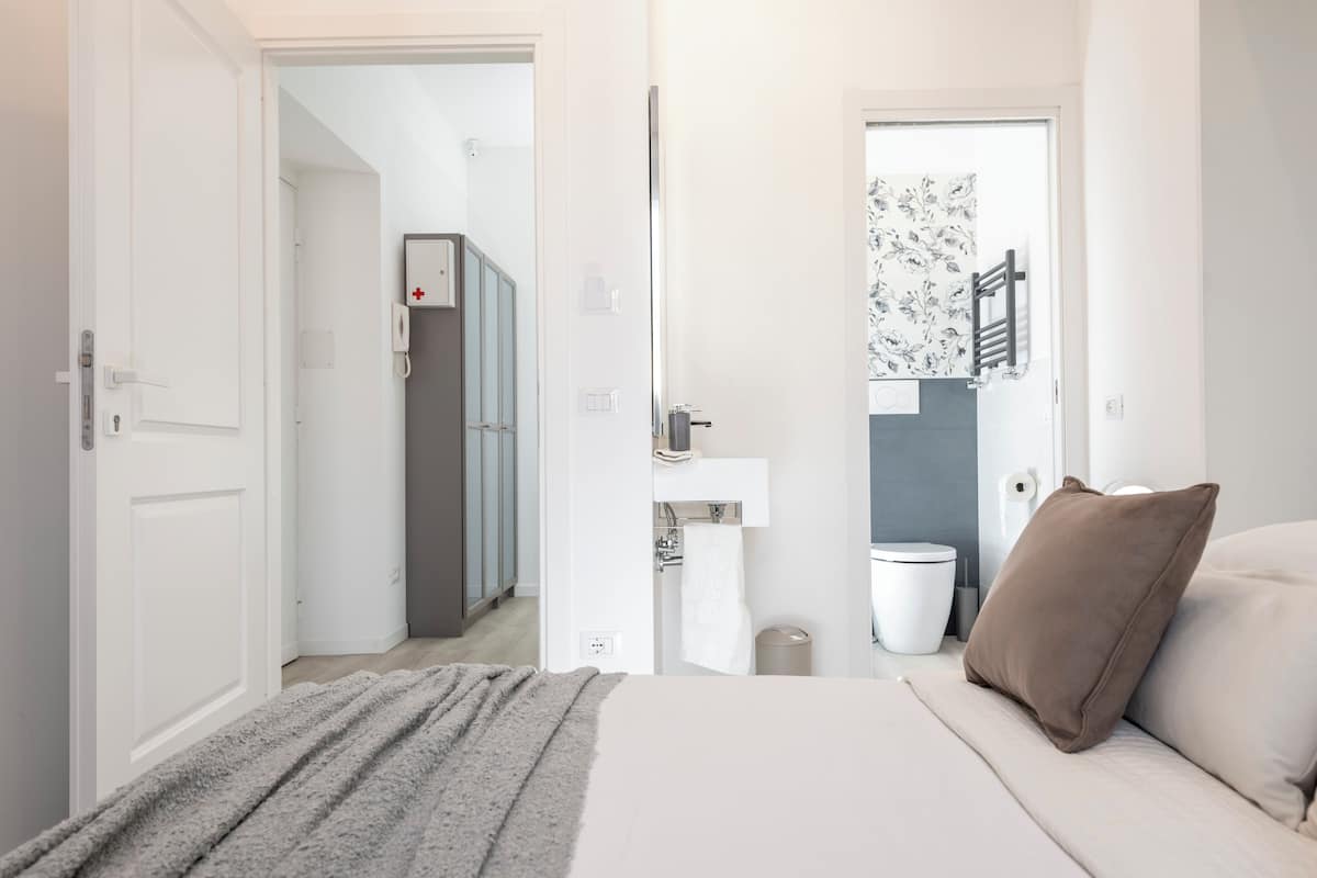 A bedroom with a bed, a bedside table, a nightstand, a window, and a door leading to a bathroom.
