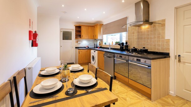 Une cuisine moderne avec des meubles en bois, des appareils en acier inoxydable et un coin repas doté d’une table en bois, mise pour quatre personnes.