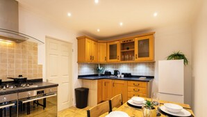 Une cuisine moderne avec des meubles en bois, une cuisinière en acier inoxydable et une table à manger pour quatre personnes.
