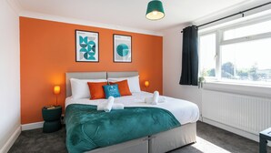 Une chambre d’hôtel avec un lit, des murs orange, une fenêtre avec des rideaux et deux tableaux encadrés accrochés au mur.