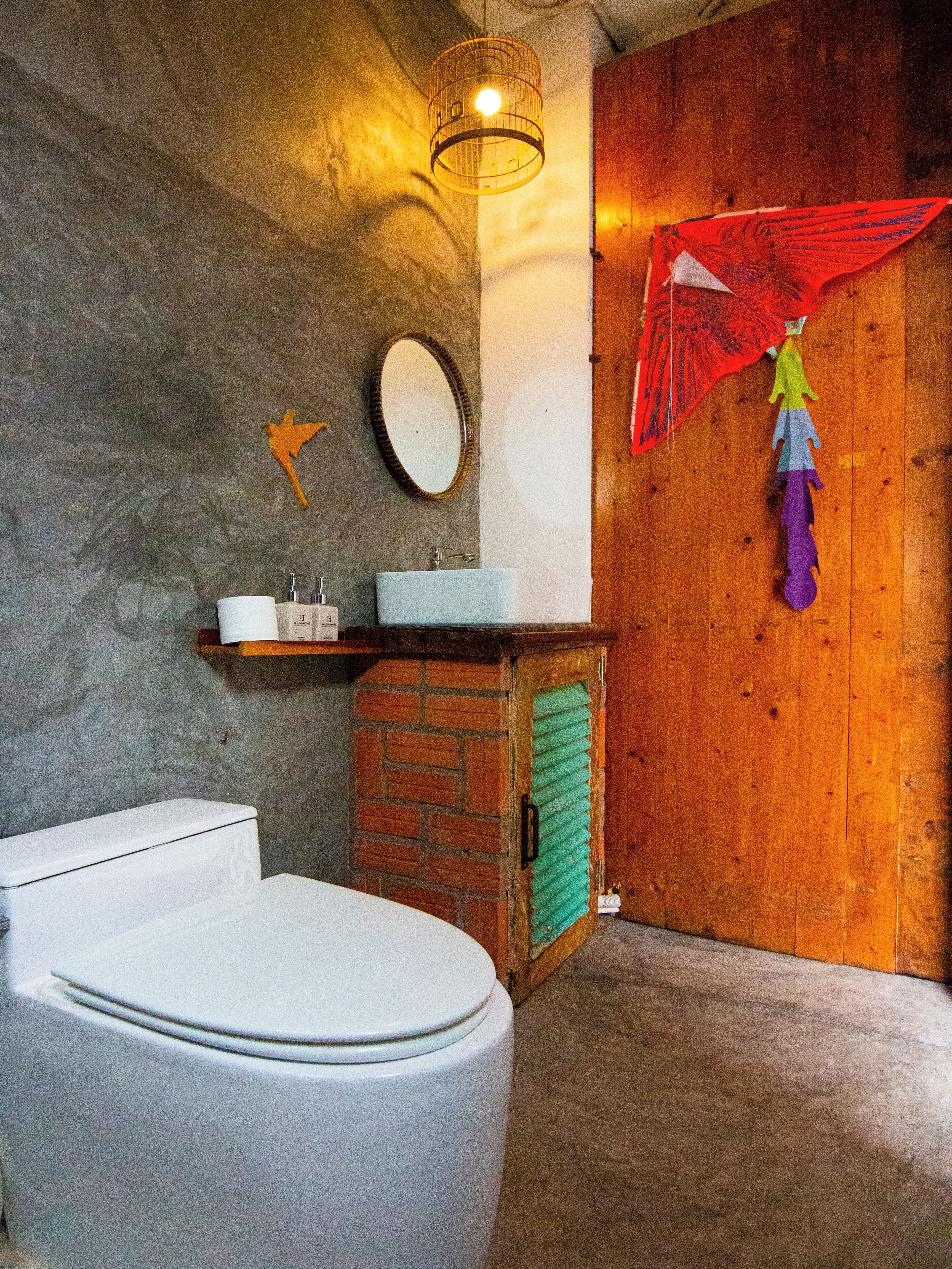 A bathroom with a toilet, sink, mirror, and a hanging decorative item.