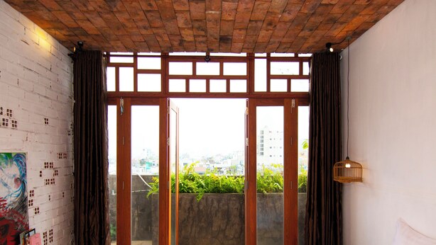 Un dormitorio con cama, escritorio, vistas a través de una puerta corrediza y techo de ladrillo.