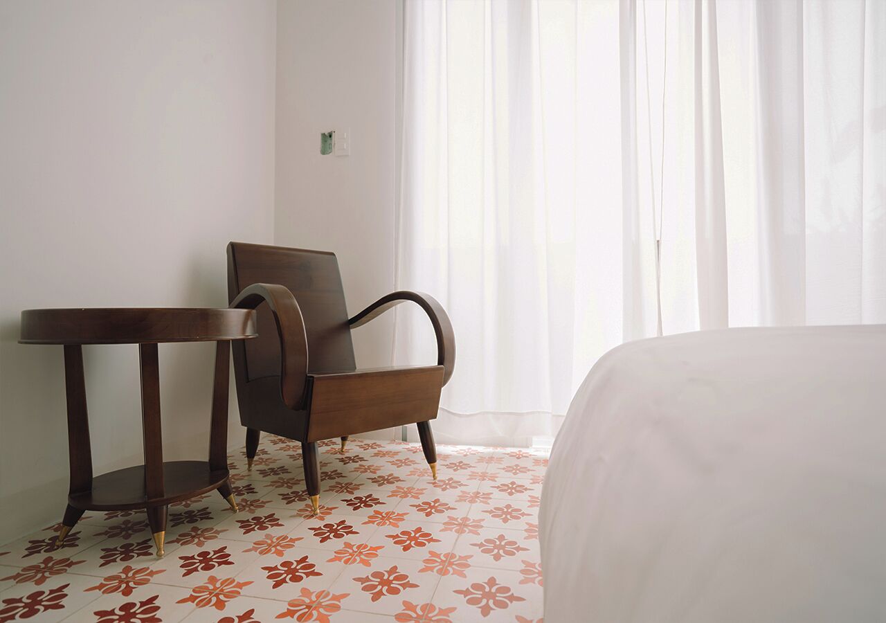 A hotel room with a bed, a wooden chair, and a small table.