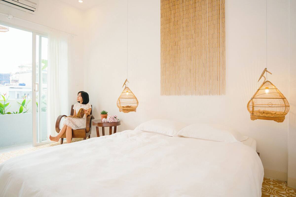 A bedroom with a large bed, a chair, a small table with a plant, and two wall-mounted birdcages.