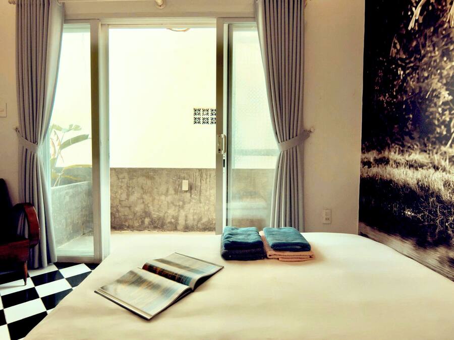 Habitación de hotel con suelo a cuadros, una cama con toallas dobladas, una revista sobre la cama y vistas a un balcón desde la puerta.