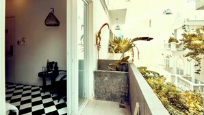 Un balcón con piso a cuadros, una lámpara colgante y vistas de un edificio blanco con balcones.