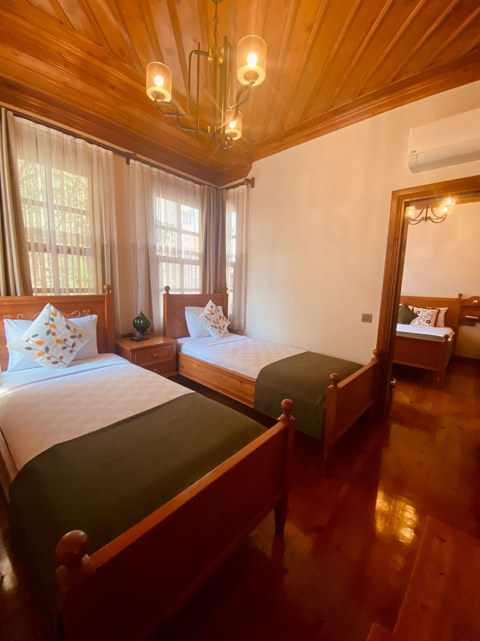 A hotel room with two wooden beds, a wooden ceiling, and a large window with curtains.
