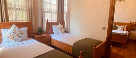 A hotel room with two wooden beds, a wooden ceiling, and a large window with curtains.
