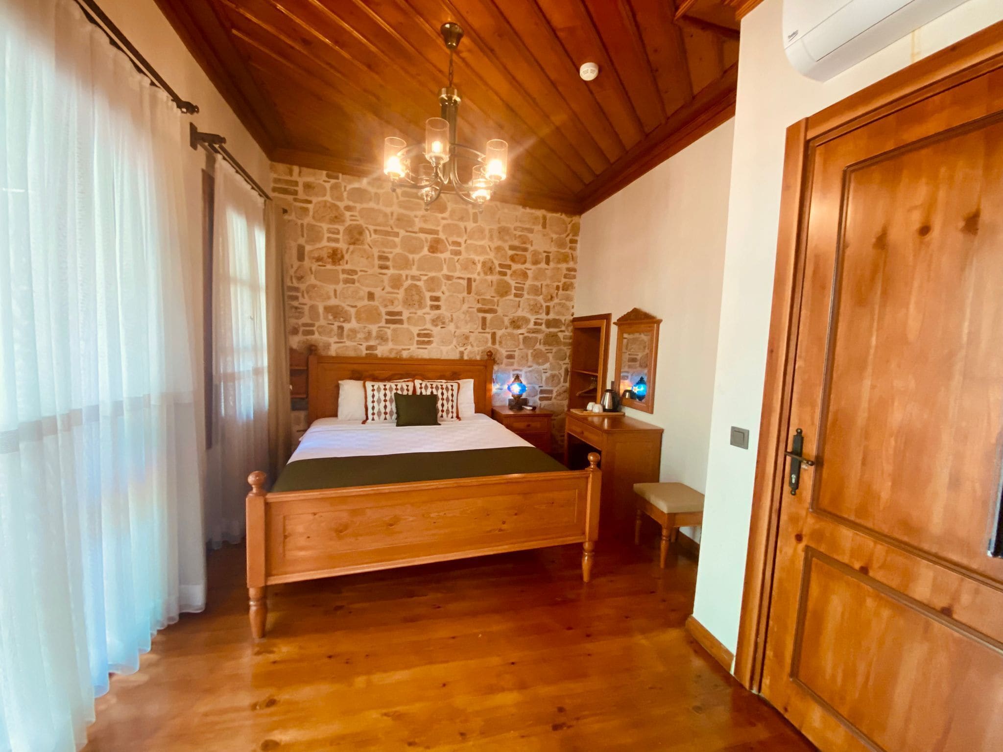 Un dormitorio con cama de madera, pared de piedra, techo de madera y una araña.