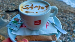 A cup of coffee with latte art on a beach with the ocean in the background. - Villa Feronia Samos (Mesokampos)