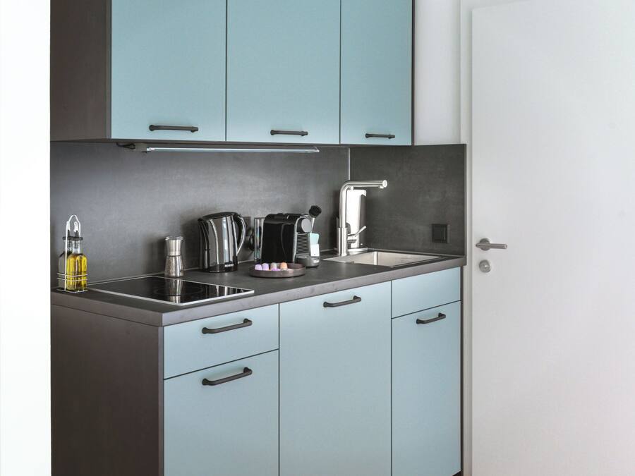 Una cocina compacta con armarios azul claro, un lavamanos de acero inoxidable y electrodomésticos modernos.