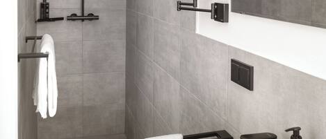 Un baño moderno con ducha a ras de suelo, un espejo grande, un lavabo blanco y un dispensador de jabón negro.