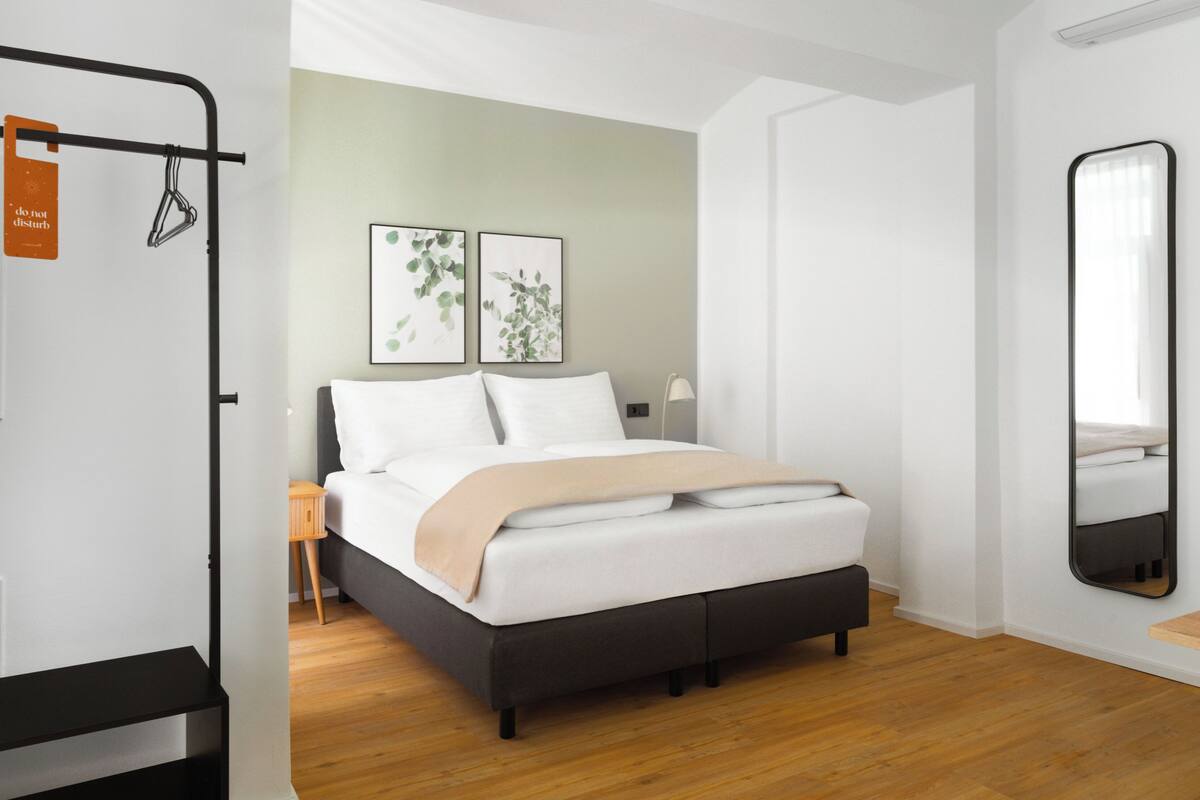 A modern bedroom with a bed, bedside table, lamp, and a large mirror.