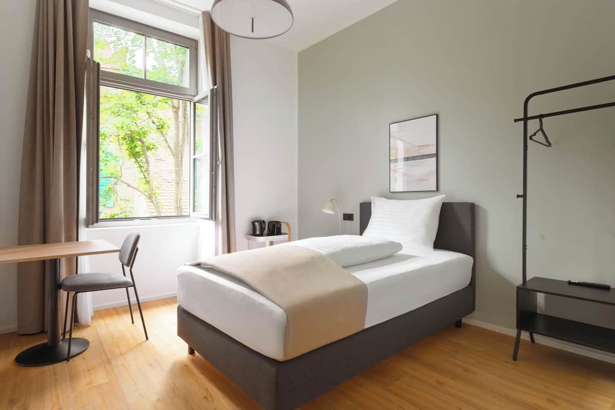 A modern hotel room with a bed, a desk, and a chair.