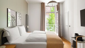 A modern hotel room with a large bed, a bedside table, a lamp, a view of greenery outside, and a balcony. - Limehome Graz Trauttmansdorffgasse (Graz)