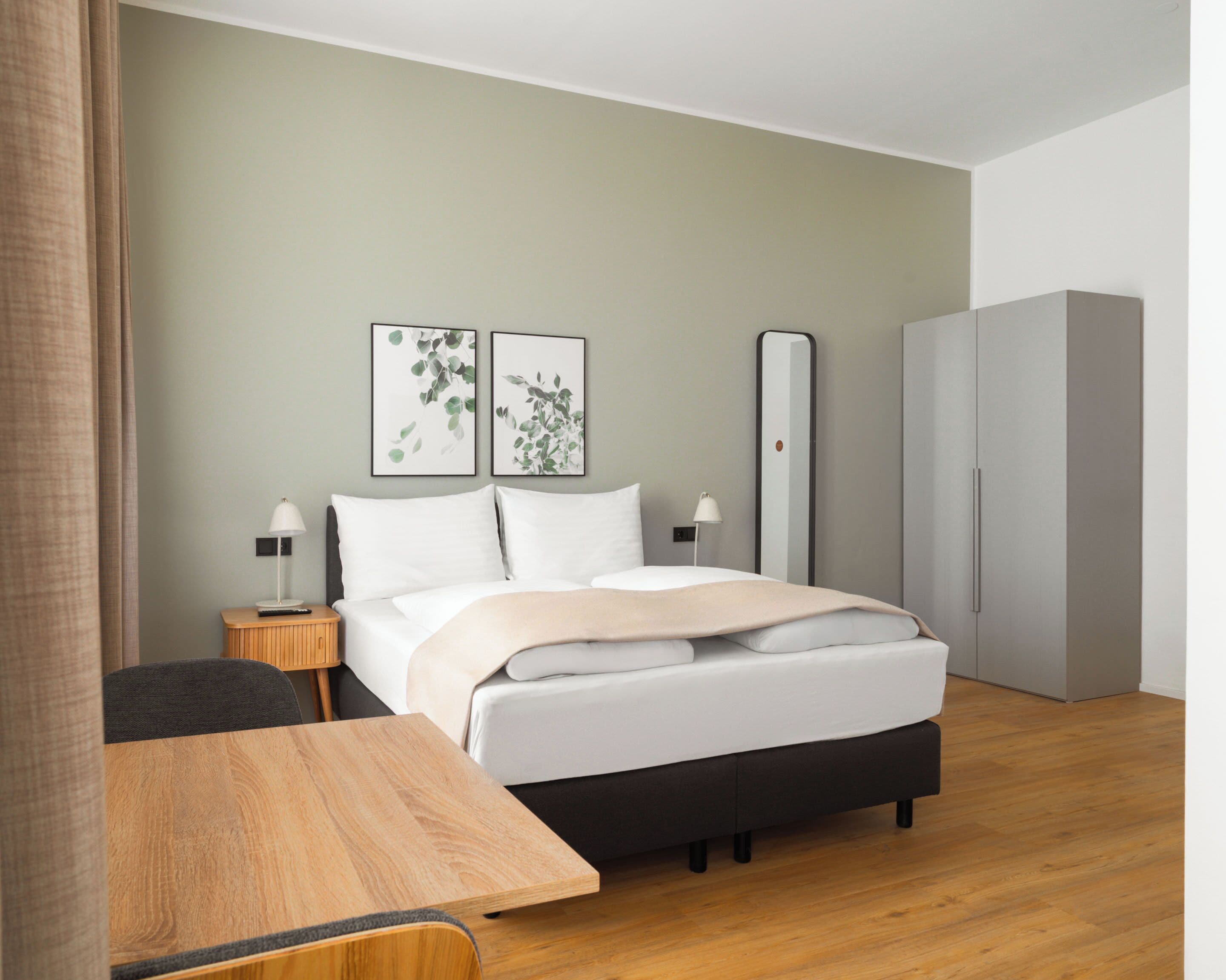 A modern hotel room with a bed, bedside tables, a mirror, and a wardrobe.