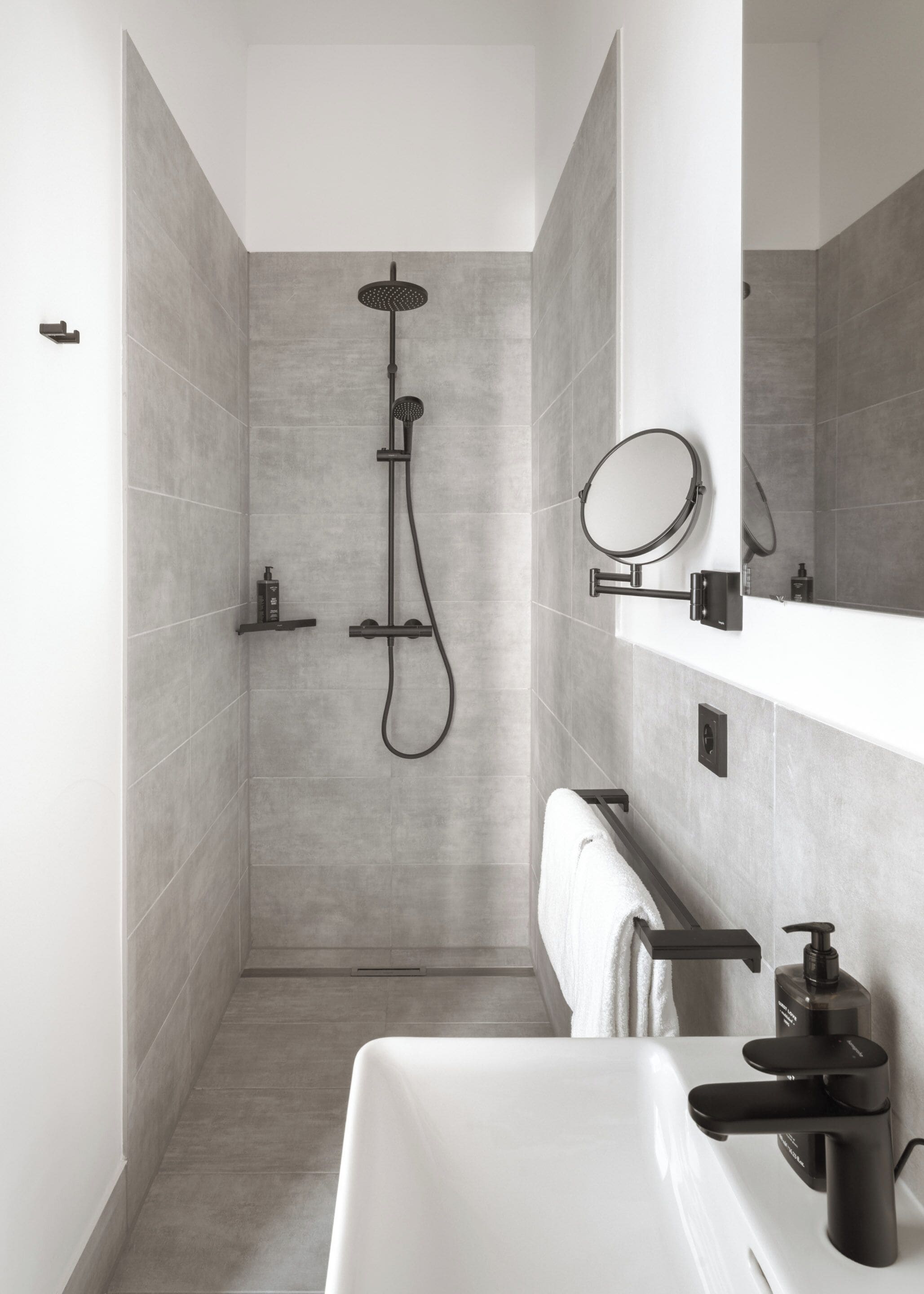 A modern bathroom with a shower, a sink, a mirror, and a towel rack.