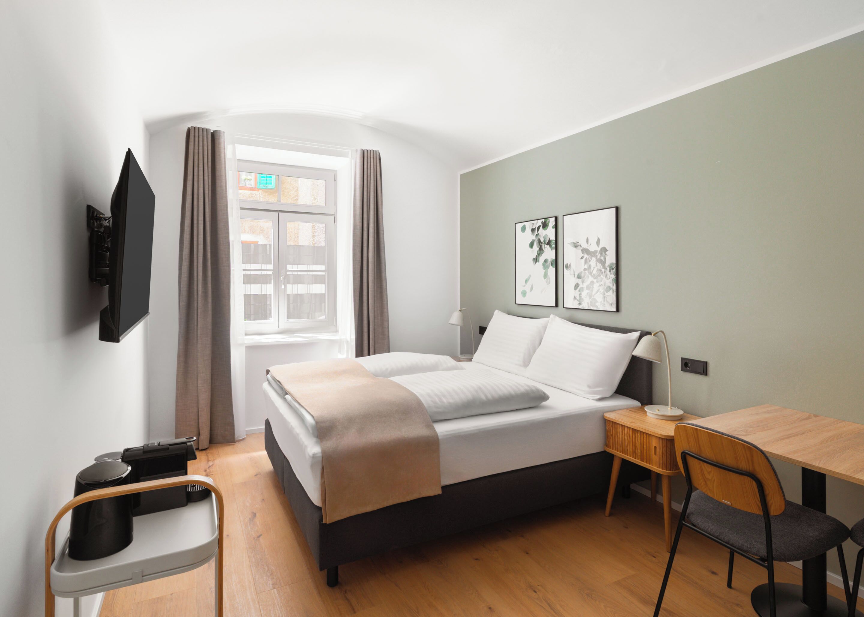 Ein modernes Hotelzimmer mit Bett, Schreibtisch, Stuhl, Wand-Fernseher und Wandkunst.