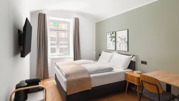 Ein modernes Hotelzimmer mit Bett, Schreibtisch, Stuhl, Wand-Fernseher und Wandkunst.