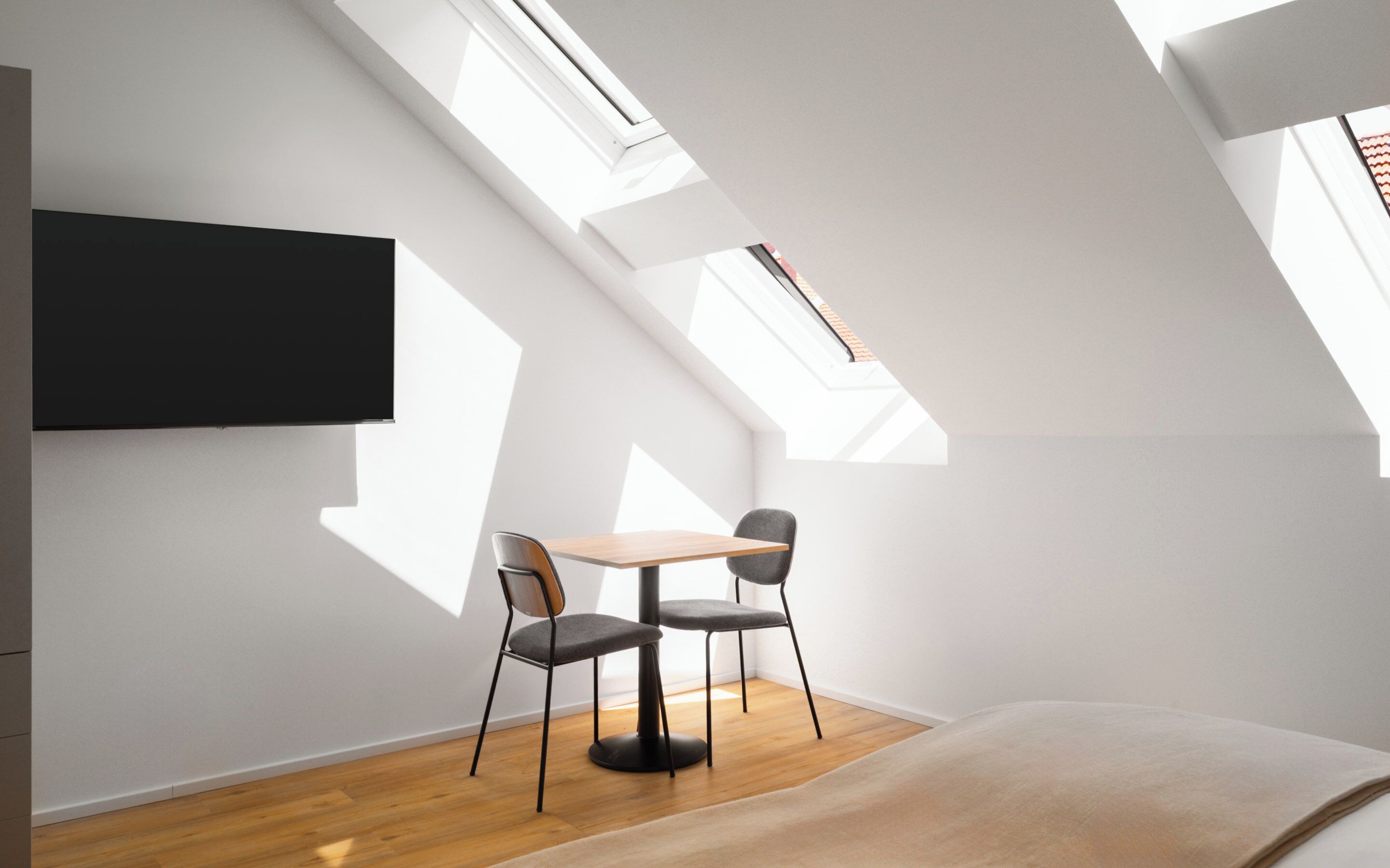Ein modernes Zimmer mit Dachfenster, einem Flachbildfernseher, einem Holztisch, zwei Stühlen und einem Bett.