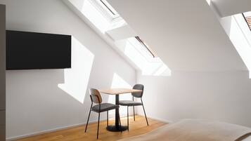 Ein modernes Zimmer mit Dachfenster, einem Flachbildfernseher, einem Holztisch, zwei Stühlen und einem Bett.