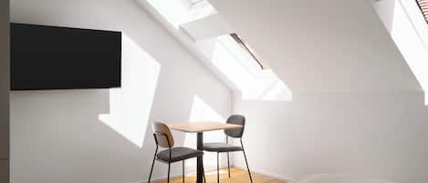 A modern room with a skylight, a flat-screen TV, a wooden table, two chairs, and a bed.