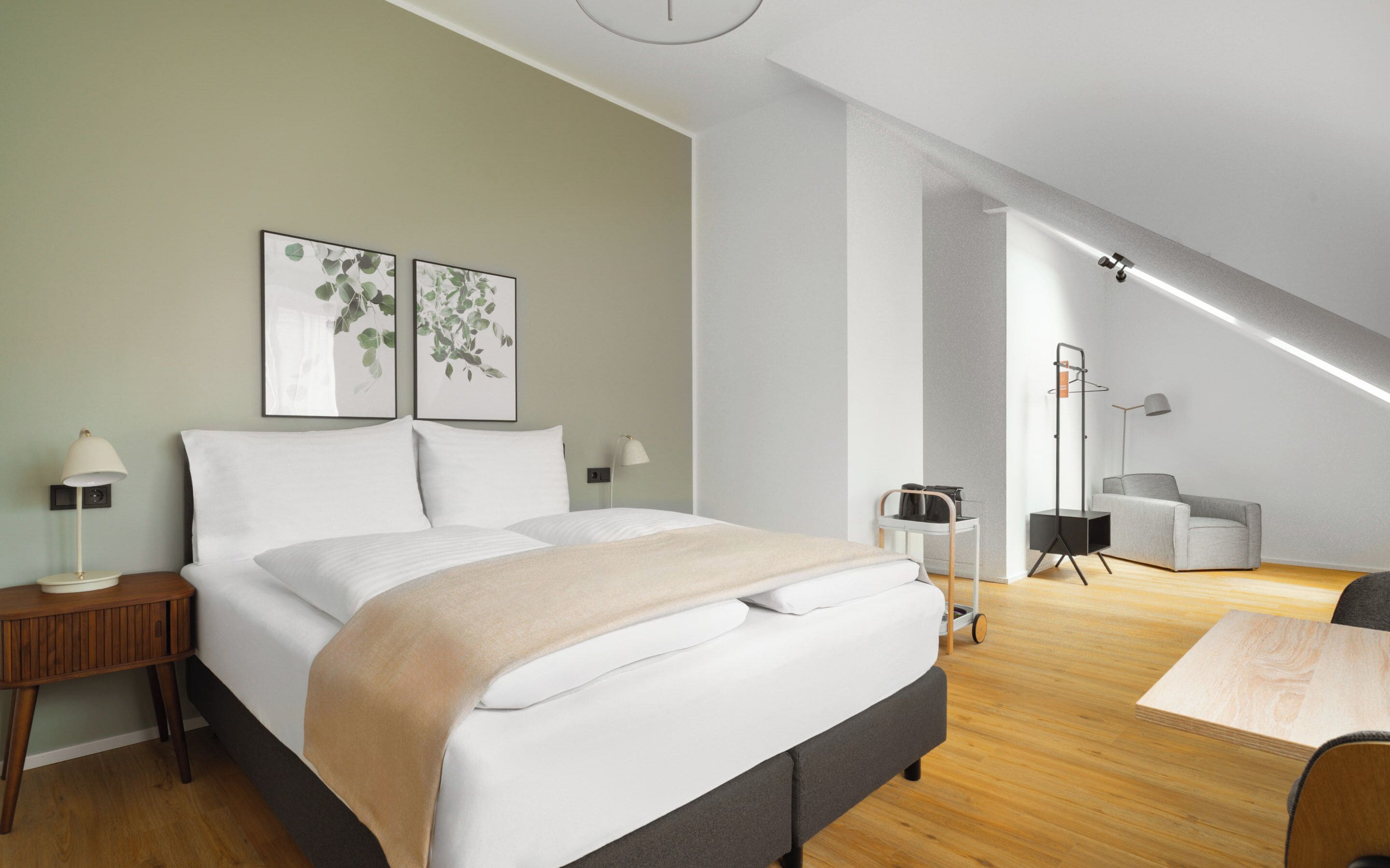 A modern bedroom with a large bed, bedside tables, a desk, and a chair. There are two framed pictures on the wall.