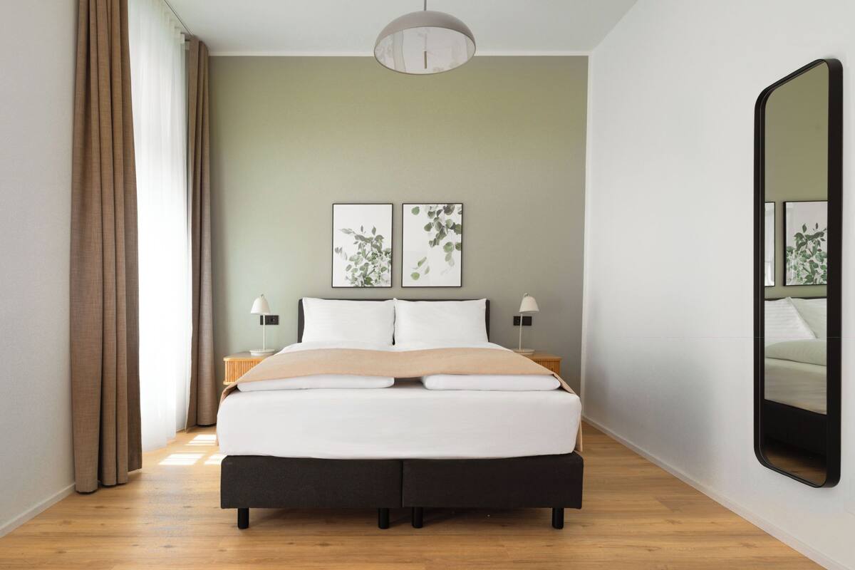 A modern bedroom with a bed, two bedside tables, a mirror, and wall art.