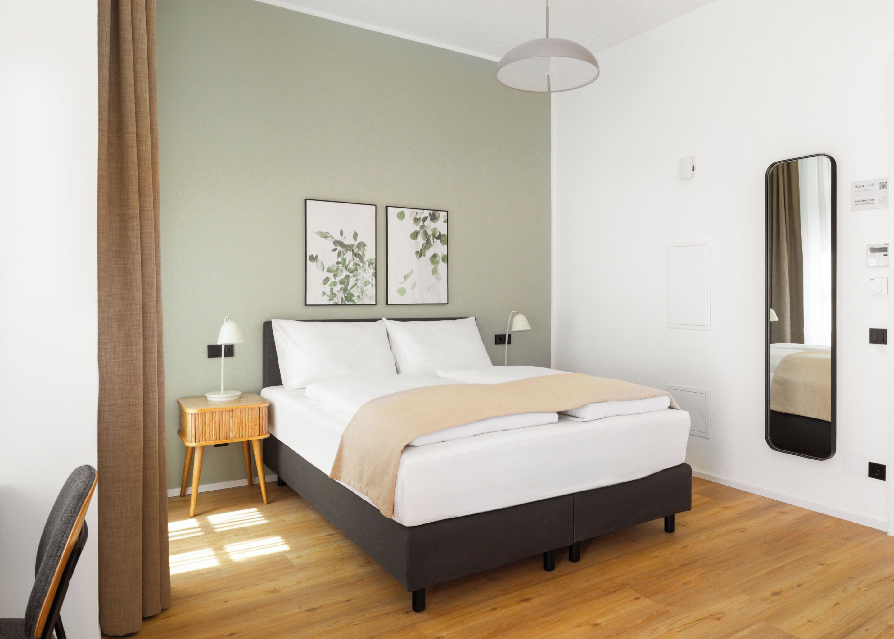 A modern bedroom with a bed, bedside tables, a mirror, and artwork on the wall.