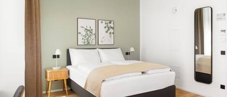 A modern bedroom with a bed, bedside tables, a mirror, and artwork on the wall.