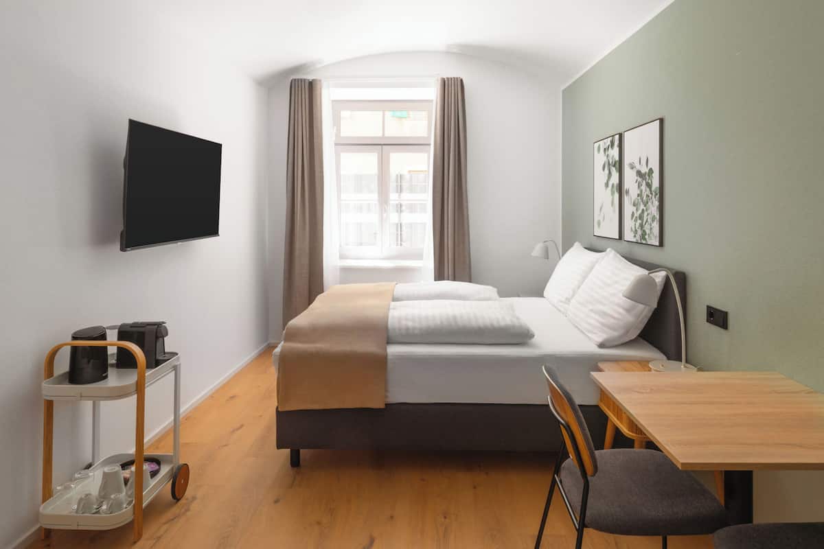 A hotel room with a bed, a desk, a chair, a TV, and a window with curtains.