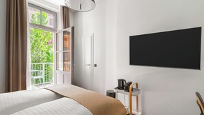 A modern bedroom with a large bed, a TV mounted on the wall, a coffee maker on a side table, and a balcony with a view of greenery. - Limehome Graz Trauttmansdorffgasse (Graz)